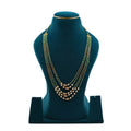 Lalithambike traditional multi-strand emerald and gold bead necklace, featuring four layers of green beads accented with white pearls and intricate gold cylindrical spacers on a teal display.
