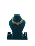 Lalithambike 1-gram gold choker featuring a row of ruby-toned stones and dangling teardrop gold accents, with matching floral earrings on a teal display.