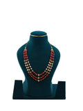 Lalithambike three-strand necklace featuring alternating deep red coral beads, cream pearls, and gold filigree accents on a teal jewelry bust.